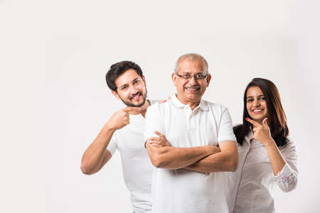 Indian old father embarrassing his young adult kids. Asian family of 3 standing isolated over white...