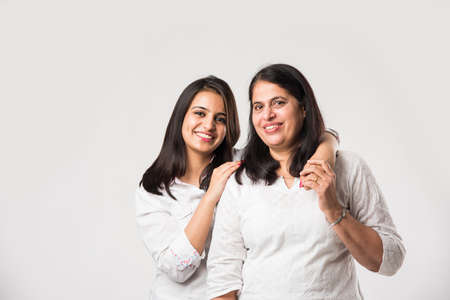 Indian old mother with young Daughter standing isolated over white background, while wearing white...