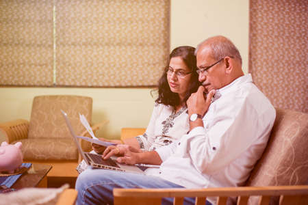 Senior Indian/asian couple accounting, doing home finance and checking bills with laptop, calculator...