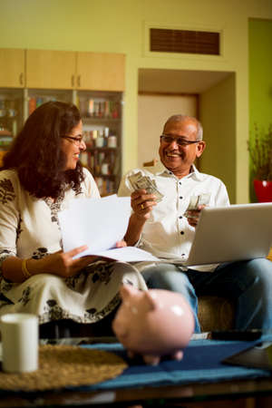Senior Indian/asian couple accounting, doing home finance and checking bills with laptop, calculator...