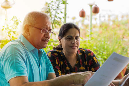 Senior Indian/asian couple accounting, doing home finance and checking bills with laptop, calculator...