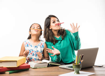 Indian girl studying with mother or teacher at study table with laptop computer, books and having fun learningの写真素材