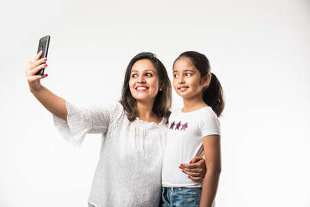 Indian/asian mother daughter taking selfie picture with smartphone, isolated over white background
