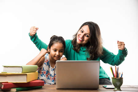 Indian girl studying with mother or teacher at study table with laptop computer, books and having fun learningの写真素材