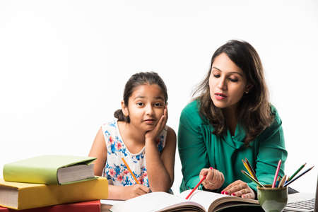 Indian girl studying with mother or teacher at study table with laptop computer, books and having fun learningの写真素材