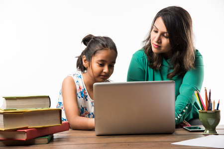 Indian girl studying with mother or teacher at study table with laptop computer, books and having...