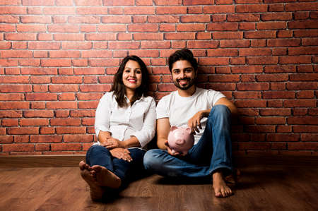 Indian couple with piggy bank standing isolated over white backgroundの写真素材