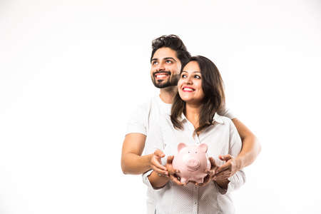 Indian couple with piggy bank standing isolated over white backgroundの写真素材