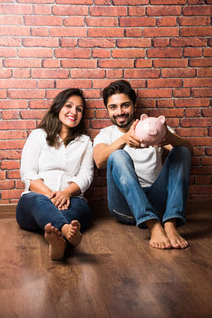 Indian couple with piggy bank standing isolated over white backgroundの写真素材