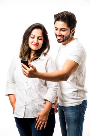 Indian couple using smartphone / mobile handset, standing isolated over white backgroundの写真素材