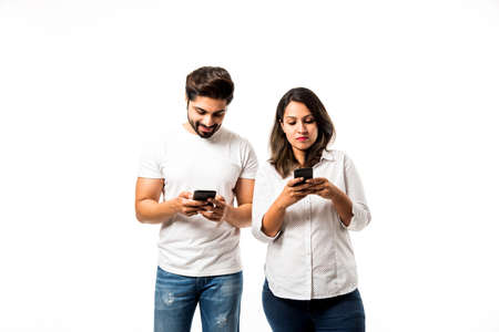 Indian couple using smartphone / mobile handset, standing isolated over white background