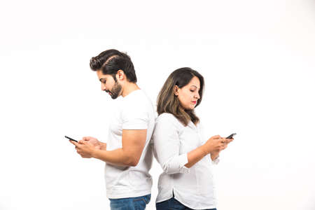 Indian couple using smartphone / mobile handset, standing isolated over white backgroundの写真素材