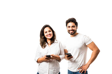 Indian couple using smartphone / mobile handset, standing isolated over white background