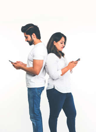 Indian couple using smartphone / mobile handset, standing isolated over white backgroundの写真素材