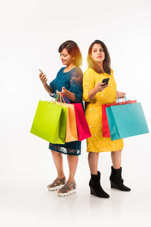 Indian Mother daughter sisters shopping with colourful bags, standing isolated over white backgroundの写真素材
