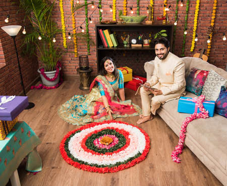 Indian couple making flower Rangoli on Diwali or Onam Festival, taking selfie or holding sweetsの写真素材