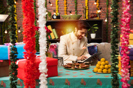 Indian man using tablet touchscreen computer on festival day while wearing traditional outfit....