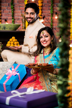 Indian couple with diya, sweets and gifts while celebrating Diwali, Deepavali or Dipavali festivalの写真素材