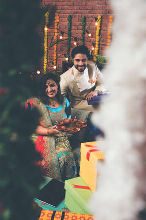 Indian couple with diya, sweets and gifts while celebrating Diwali, Deepavali or Dipavali festival