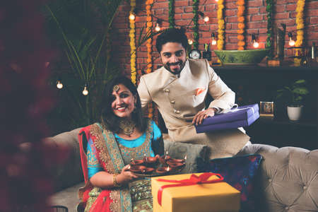 Indian couple with diya, sweets and gifts while celebrating Diwali, Deepavali or Dipavali festival