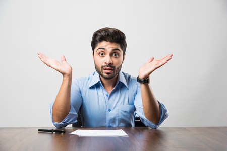 Stressed Indian Businessman having headache or Migraine pain while working at office tableの写真素材