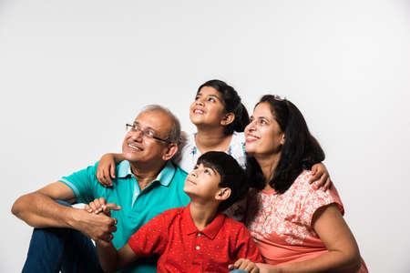 Indian Kids with grandparents smiling while sitting on a white background indoors, selective focus