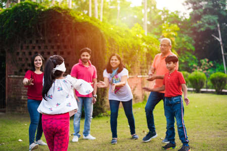 Indian Family playing blindfold game in park or garden, multi generation asian family playing...
