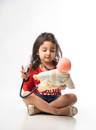 Indian Little child girl with stethoscope and Stuffed Baby or Puppy toy sitting against white backgroundの写真素材