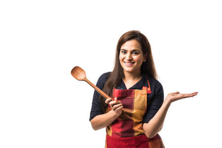 Indian / asian woman chef wearing Apron and holding wooden spatula while standing isolated over white backgroundの写真素材