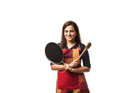 Indian / asian woman chef wearing Apron and holding Pan and spatula while standing isolated over white backgroundの写真素材