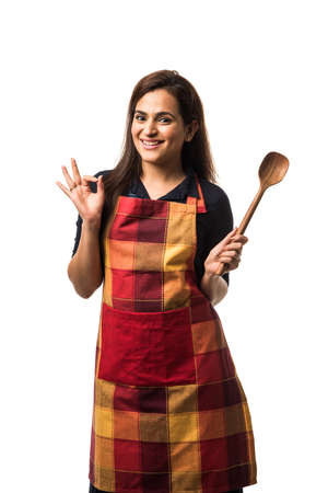 Indian / asian woman chef wearing Apron and holding wooden spatula while standing isolated over white backgroundの写真素材