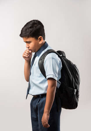 Indian school boy coughing while wearing school uniform and schoolbag, isolated over whiteの写真素材