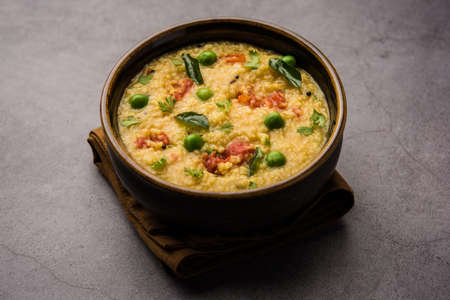 Vegetable Dalia or Daliya Khichadi or Broken Wheat Khichdi with tomato, green peas and chilli, served in a bowl or plateの写真素材