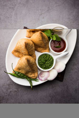 Samosa - Triangle shape fried / baked pastry with savoury filling, popular Indian Tea Time snacks, served with green chutney, tomato ketchupの写真素材