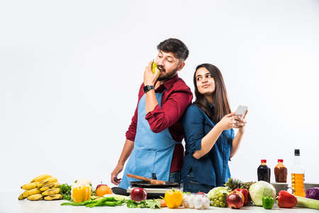 Indian couple in kitchen - Young Beautiful asian wife enjoying cooking with husband with lots of fresh vegetables and fruitsの写真素材