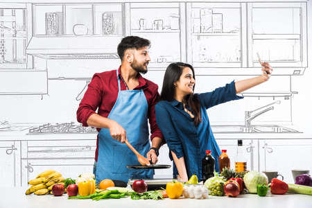Indian couple in kitchen - Young Beautiful asian wife enjoying cooking with husband with lots of...