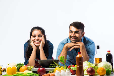 Indian couple in kitchen - Young Beautiful asian wife enjoying cooking with husband with lots of fresh vegetables and fruitsの写真素材