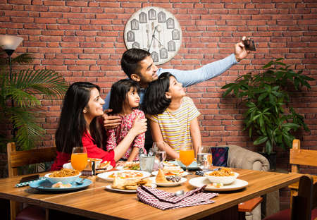 Indian young Family of four eating food at dining table at home or in restaurant. South Asian...