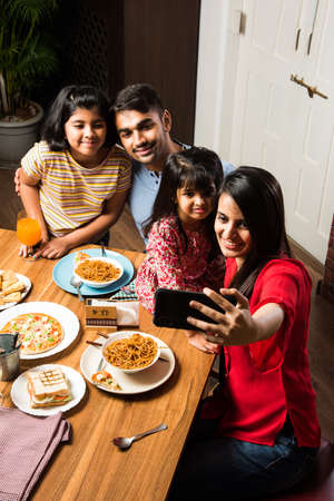 Indian young Family of four eating food at dining table at home or in restaurant. South Asian...