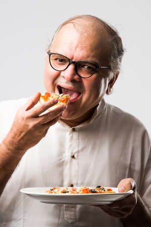 Indian asian senior or old man eating pizza while standing isolated against white backgroundの写真素材