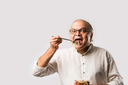 Senior Indian asian man eating fresh green salad. Mature male male having healthy snack, healthcare,...