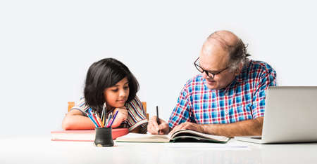Indian grandfather teaching granddaughter with books, pencil and laptop, home schooling or tuition