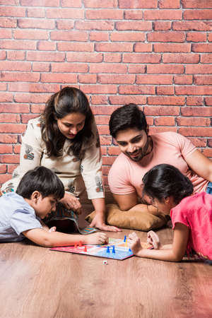 Indian young family of four playing board games like Chess, Ludo or Snack and Ladder at home in quarantineの写真素材