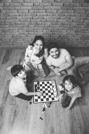 Indian young family of four playing board games like Chess, Ludo or Snack and Ladder at home in quarantineの写真素材