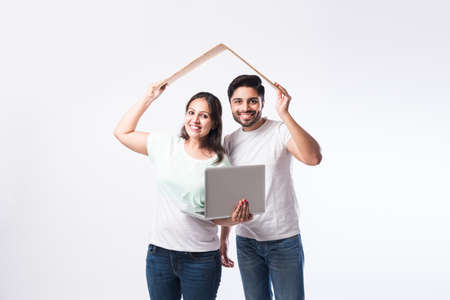 Indian young family couple choosing new home online, search real estate to buy or rent, house for sale on screen of computer, standing against white backgroundの写真素材
