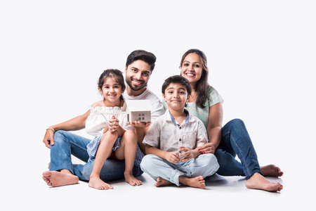 Indian family Father, mother, son and daughter holding 3D paper model of home - Real Istate Concept...