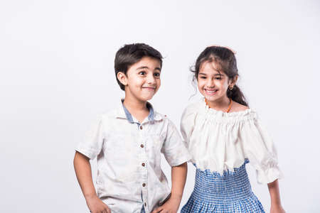 Cute little Indian asian siblings standing and embracing each other in white clothes while standing againstwhite background.の写真素材