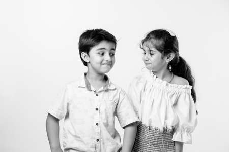 Cute little Indian asian siblings standing and embracing each other in white clothes while standing...