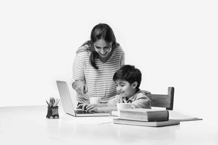 Cute Indian boy with mother doing homework at home using laptop and books - online schooling conceptの写真素材