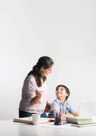 Cute Indian boy with mother doing homework at home using laptop and books - online schooling concept